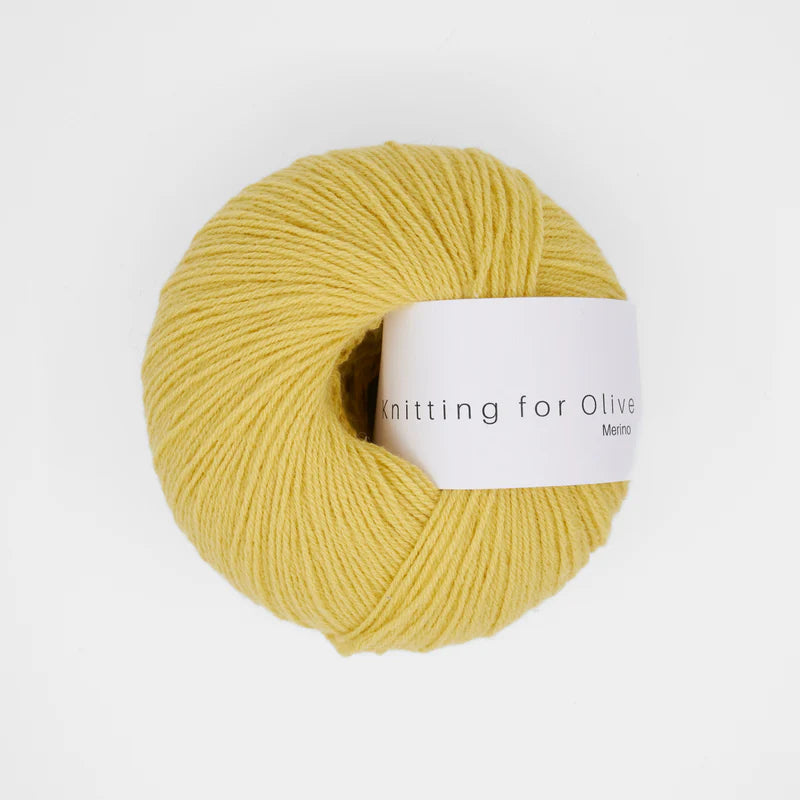 “Bol wol in de kleur ‘Buttercup’ van Knitting for Olive, uit de Merino-lijn, netjes opgerold met wit label tegen een witte achtergrond – zacht, ademend en duurzaam garen.”