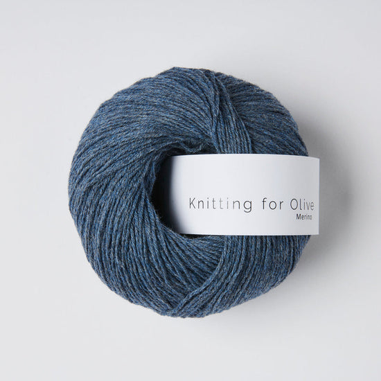 “Bol wol in de kleur ‘Blue Jeans’ van Knitting for Olive, uit de Merino-lijn, netjes opgerold met wit label tegen een witte achtergrond – zacht, ademend en duurzaam garen."