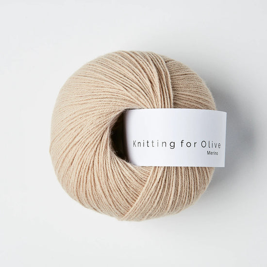 “Bol wol in de kleur ‘Powder’ van Knitting for Olive, uit de Merino-lijn, elegant opgerold met wit label tegen een witte achtergrond – zacht, licht en perfect voor fijne breiprojecten.”