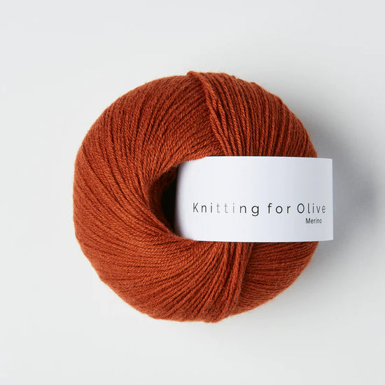 “Bol wol in de kleur ‘Rust’ van Knitting for Olive, uit de Merino-lijn, netjes opgerold met wit label tegen een witte achtergrond – zacht, ademend en duurzaam garen.”
