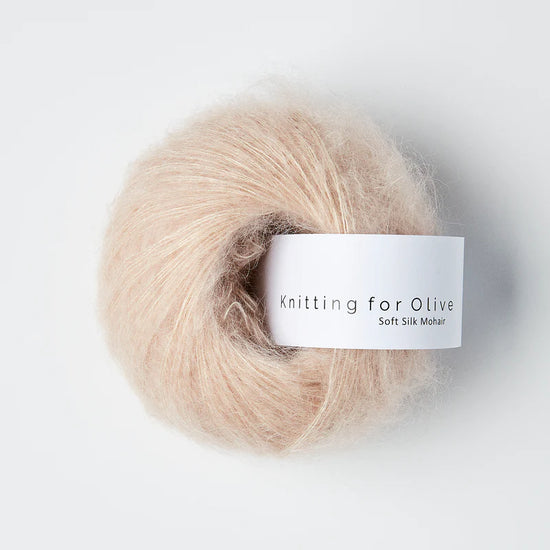 “Bol wol in de kleur ‘Soft Rose’ van Knitting for Olive, uit de Soft Silk Mohair-lijn, pluizig en luchtig opgerold met een wit label tegen een witte achtergrond – luxe en duurzaam garen van mohair en zijde.”