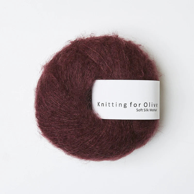 “Bol wol in de kleur ‘Bordeaux’ van Knitting for Olive, uit de Soft Silk Mohair-lijn, pluizig en luchtig opgerold met een wit label tegen een witte achtergrond – luxe en duurzaam garen van mohair en zijde.”