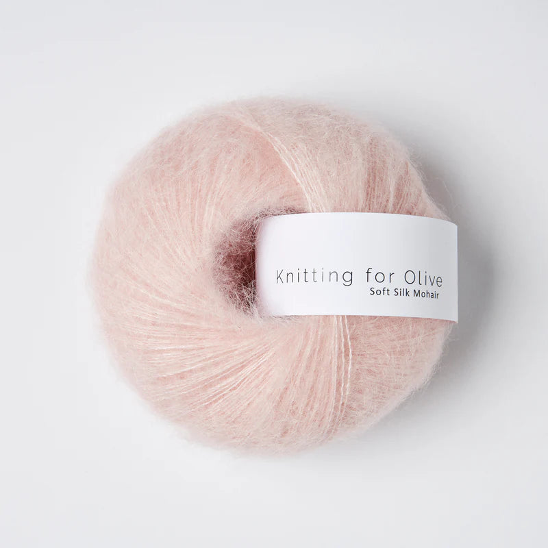 “Bol wol in de kleur ‘Cherry Blossom’ van Knitting for Olive, uit de Soft Silk Mohair-lijn, pluizig en luchtig opgerold met een wit label tegen een witte achtergrond – luxe en duurzaam garen van mohair en zijde.”