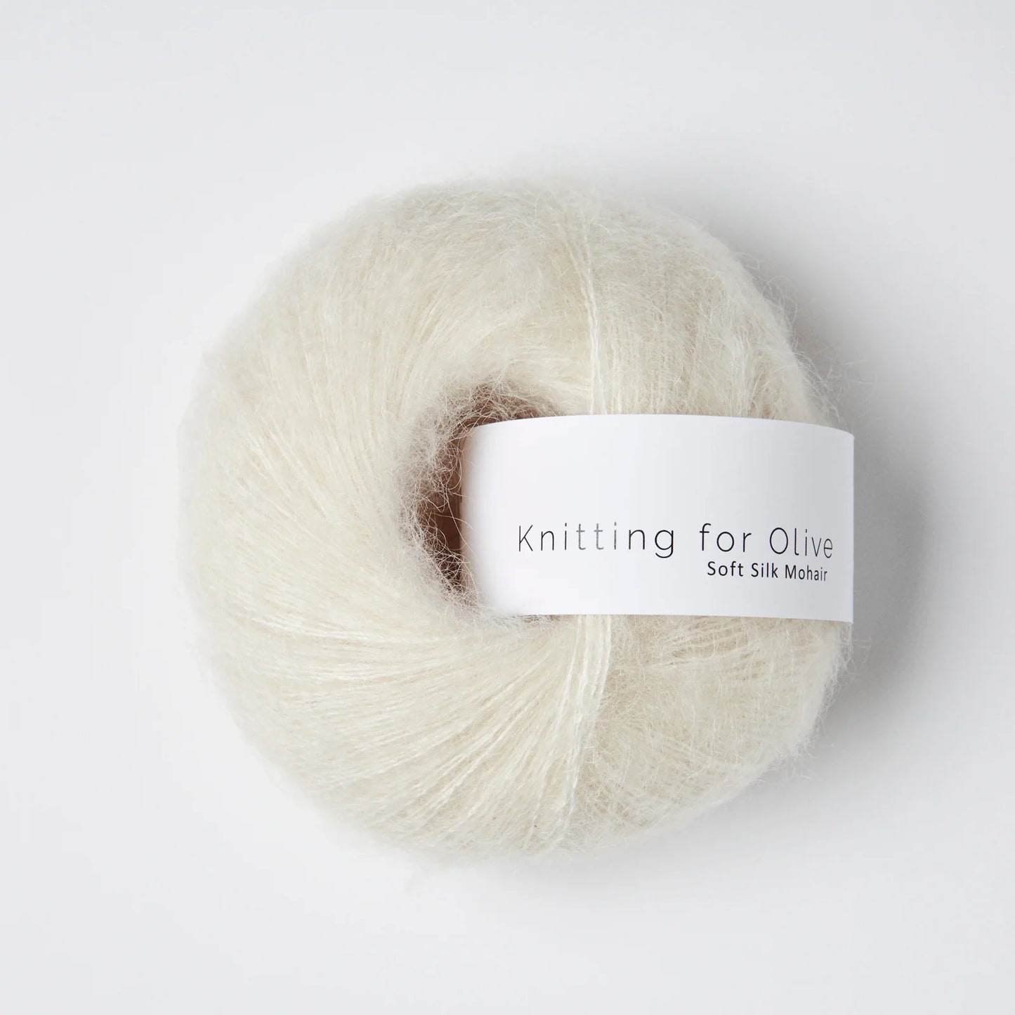“Bol wol in de kleur ‘Cream’ van Knitting for Olive, uit de Soft Silk Mohair-lijn, luchtig en zijdeachtig opgerold met een wit label tegen een witte achtergrond – elegant en diervriendelijk garen in een zachte crèmetint.”