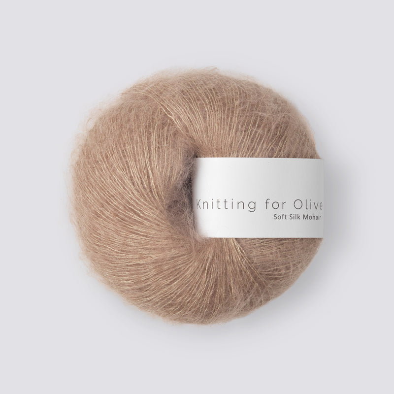 “Bol wol in de kleur ‘Sparrow’ van Knitting for Olive, uit de Soft Silk Mohair-lijn, elegant pluizig en licht glanzend met wit label tegen een witte achtergrond – luxueus garen van mohair en cruelty free zijde.”