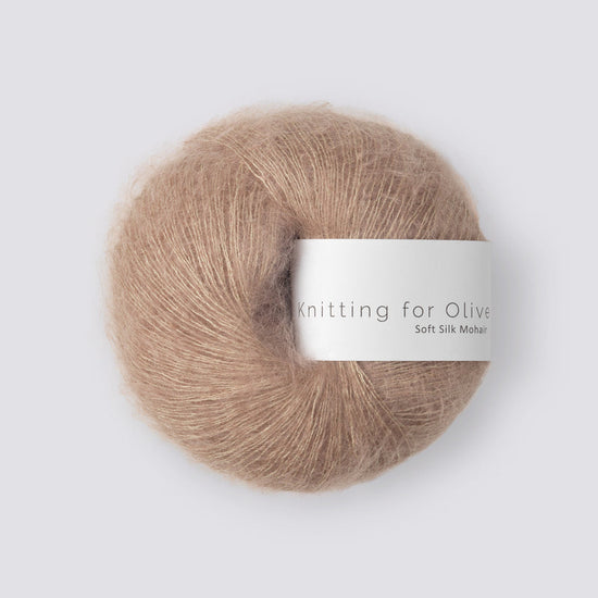 “Bol wol in de kleur ‘Sparrow’ van Knitting for Olive, uit de Soft Silk Mohair-lijn, elegant pluizig en licht glanzend met wit label tegen een witte achtergrond – luxueus garen van mohair en cruelty free zijde.”