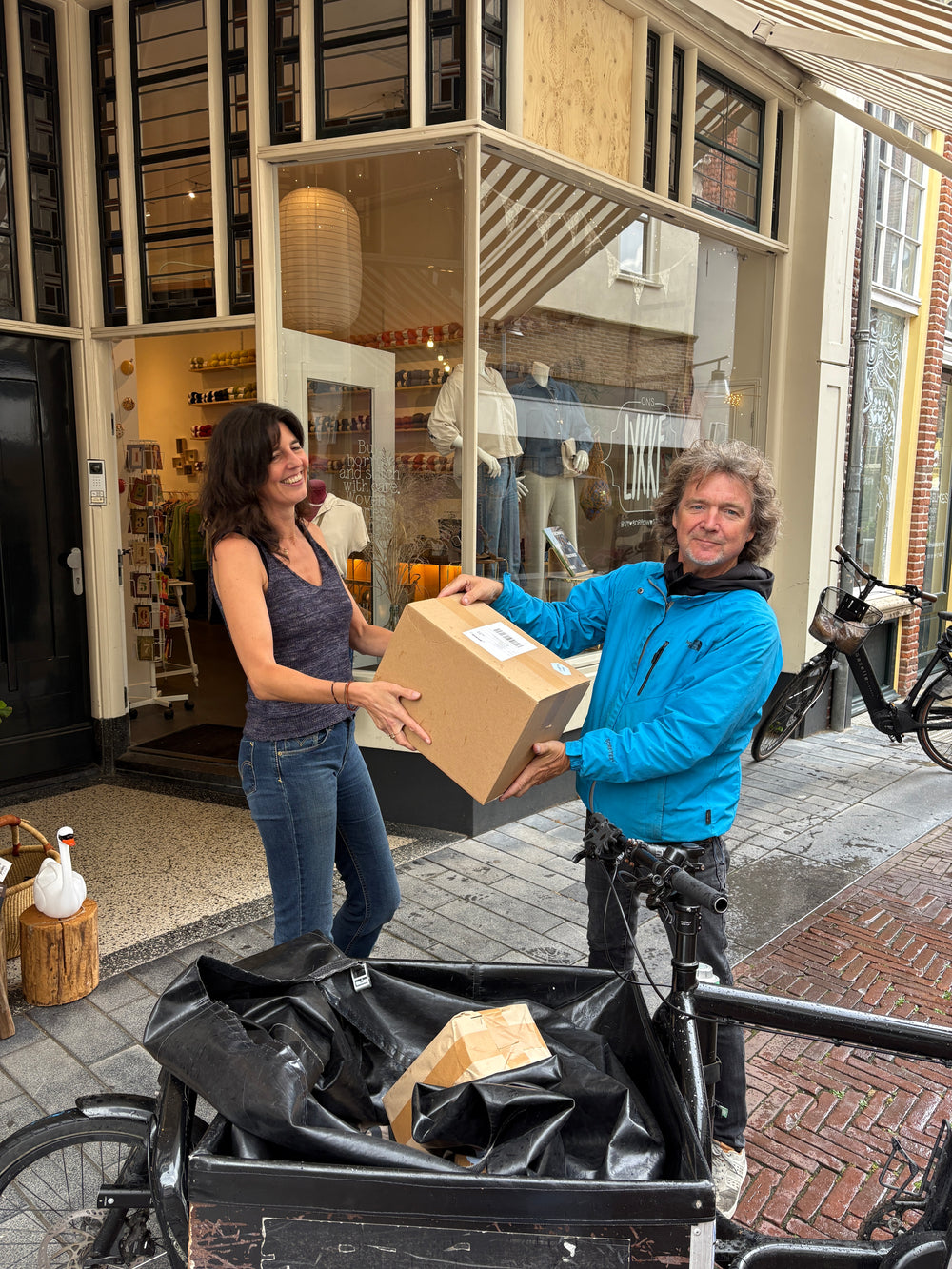 Christel van Ons Lykke overhandigt een pakket aan de fietskoerier — duurzame verzending vanuit de wolwinkel in Zutphen.