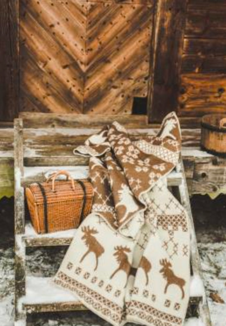 Belpo wollen plaid in bruin en beige met kerstpatroon, uitgestald op een houten trap bij een rustieke schuur in winterse sfeer.