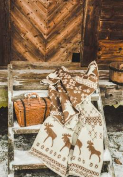 Belpo wollen plaid in bruin en beige met kerstpatroon, uitgestald op een houten trap bij een rustieke schuur in winterse sfeer.