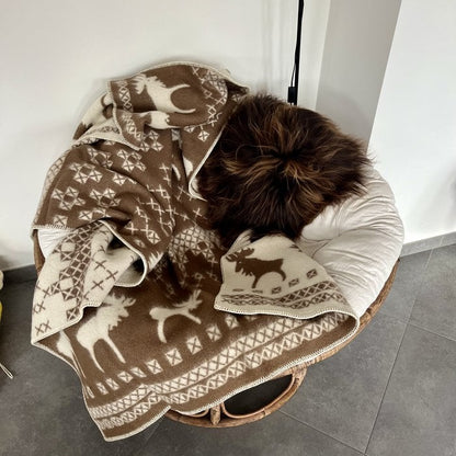 Bruin-beige kerstplaid met rendieren en sneeuwvlokkenmotief, nonchalant gedrapeerd over een ronde stoel met witte kussens