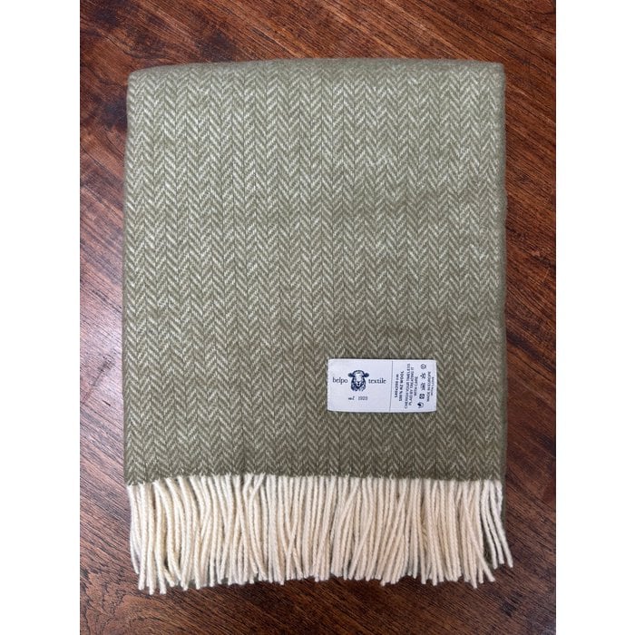 Groen wollen plaid met visgraatpatroon en witte franjes, op houten vloer met zichtbaar Belpo Textile-label.