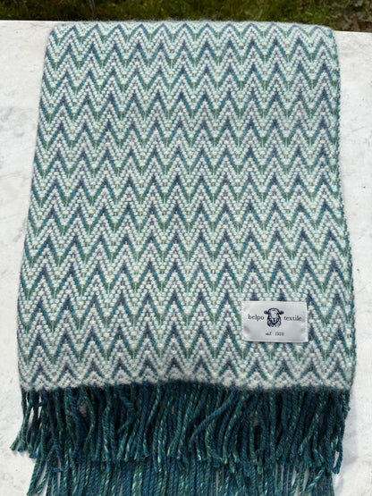 Gevouwen blauw-wit plaid van wol met zigzagweefsel en franjes, liggend op marmeren ondergrond. Het label van Belpo Textile is goed zichtbaar.