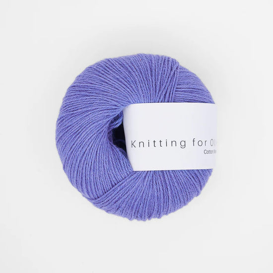 Bol wol in de kleur ‘Lavender Blue’ van Knitting for Olive, uit de Cotton Merino-collectie, netjes opgerold met een wit label en weergegeven tegen een rustige witte achtergrond – perfect voor zachte en tijdloze breiprojecten.