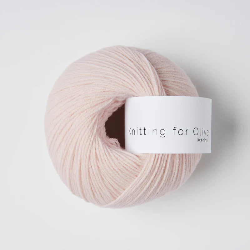 “Bol wol in de kleur ‘Ballerina’ van Knitting for Olive, uit de Merino-lijn, netjes opgerold met wit label tegen een witte achtergrond – zacht, ademend en duurzaam garen.”