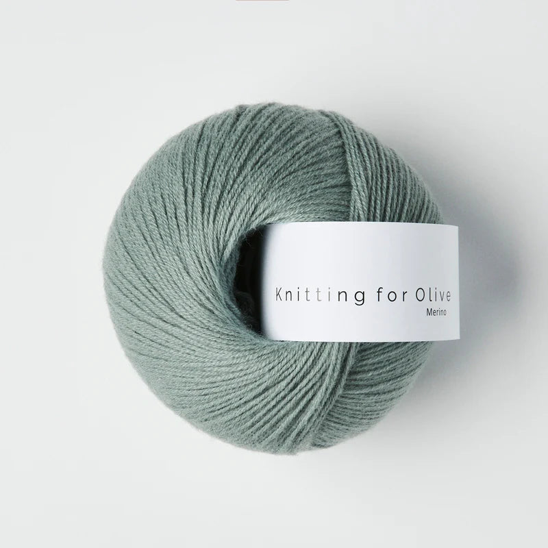 “Bol wol in de kleur ‘Dusty Aqua’ van Knitting for Olive, uit de Merino-lijn, netjes opgerold met wit label tegen een witte achtergrond – zacht, ademend en duurzaam garen.”