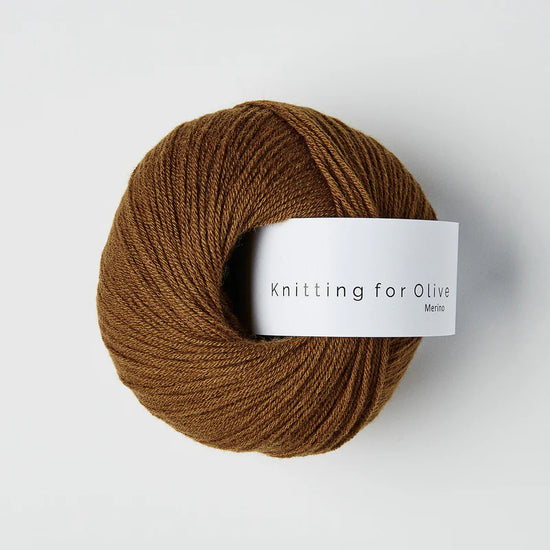 “Bol wol in de kleur ‘Ochre Brown’ van Knitting for Olive, uit de Merino-lijn, netjes opgerold met wit label tegen een witte achtergrond – zacht, ademend en duurzaam garen.”