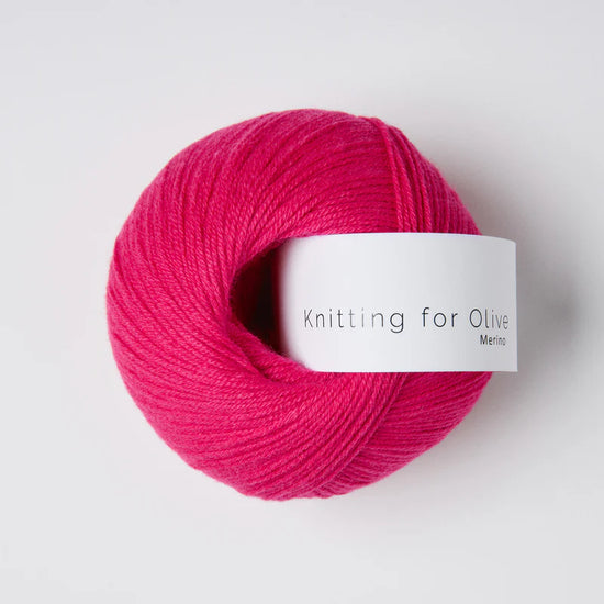 “Bol wol in de kleur ‘Pink Daisies’ van Knitting for Olive, uit de Merino-lijn, netjes opgerold met wit label tegen een witte achtergrond – zacht, ademend en duurzaam garen.”