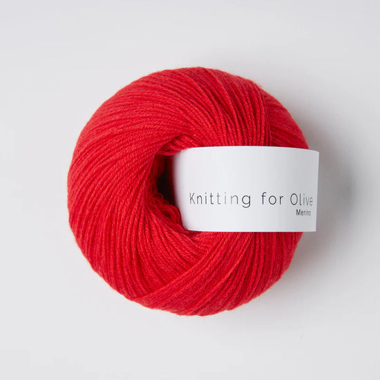 “Bol wol in de kleur ‘Redcurrant’ van Knitting for Olive, uit de Merino-lijn, netjes opgerold met wit label tegen een witte achtergrond – zacht, ademend en duurzaam garen.”