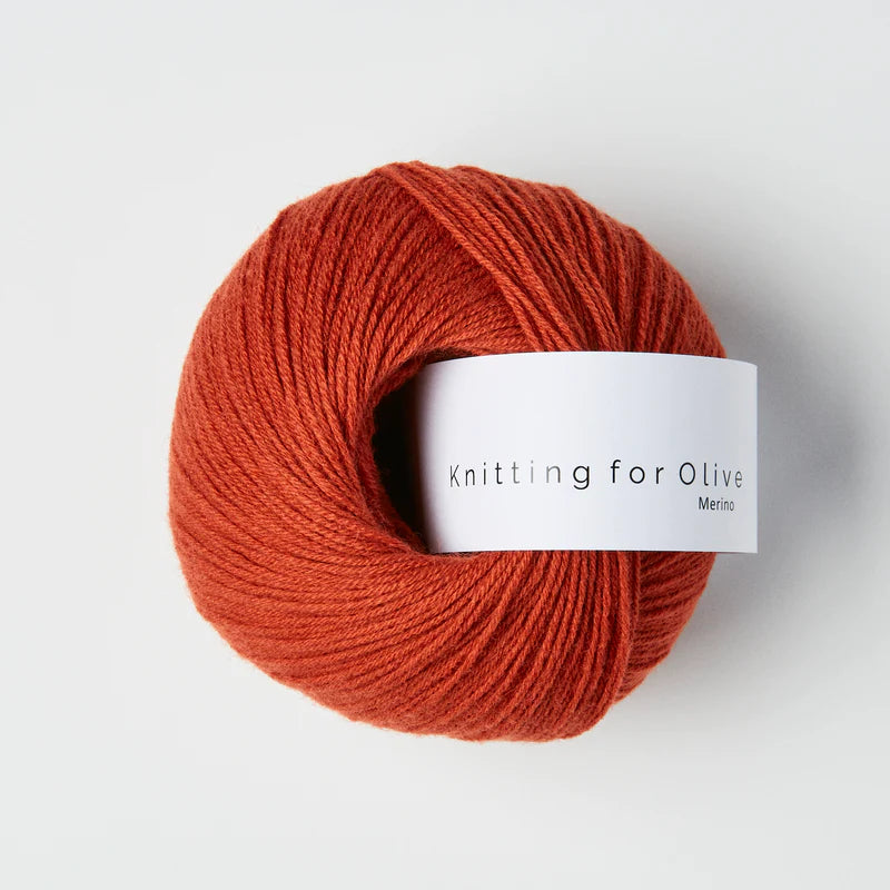 “Bol wol in de kleur ‘Robin’ van Knitting for Olive, uit de Merino-lijn, netjes opgerold met wit label tegen een witte achtergrond – zacht, ademend en duurzaam garen.”