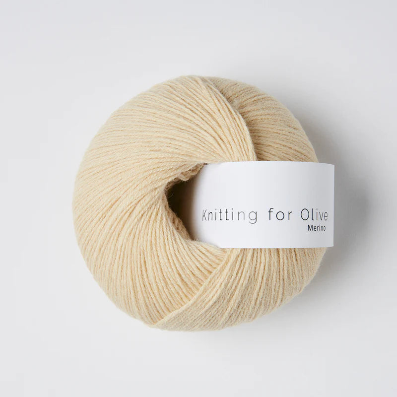“Bol wol in de kleur ‘Wheat’ van Knitting for Olive, uit de Merino-lijn, netjes opgerold met wit label tegen een witte achtergrond – zacht, ademend en duurzaam garen.”