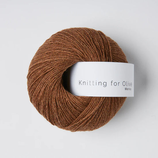 “Bol wol in de kleur ‘Dark Cognac’ van Knitting for Olive, uit de Merino-lijn, netjes opgerold met wit label tegen een witte achtergrond – zacht, ademend en verantwoord garen.”