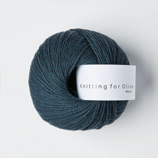 “Bol wol in de kleur ‘Deep Petroleum Blue’ van Knitting for Olive, uit de Merino-lijn, netjes opgerold met wit label tegen een witte achtergrond – zacht, ademend en duurzaam garen.”