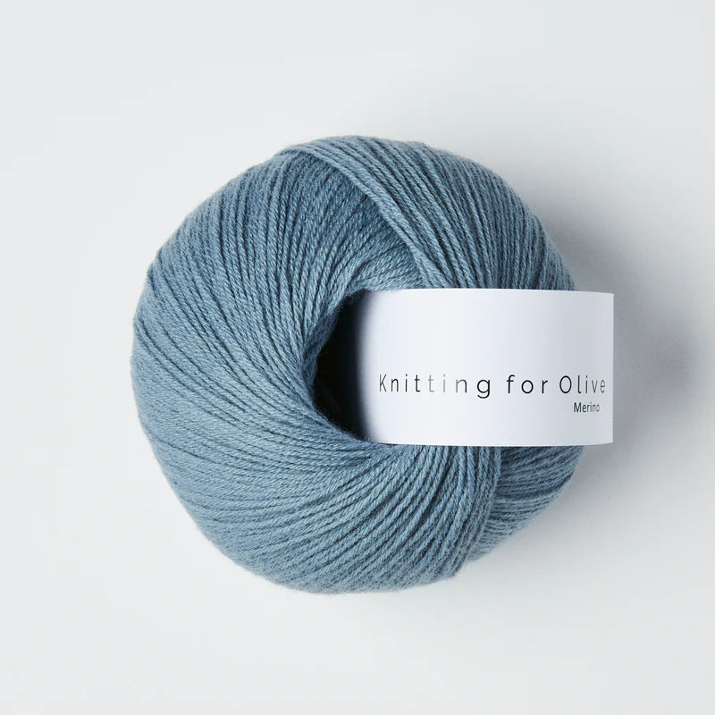 “Bol wol in de kleur ‘Dusty Dove Blue’ van Knitting for Olive, uit de Merino-lijn, netjes opgerold met wit label tegen een witte achtergrond – zacht, ademend en duurzaam garen.”