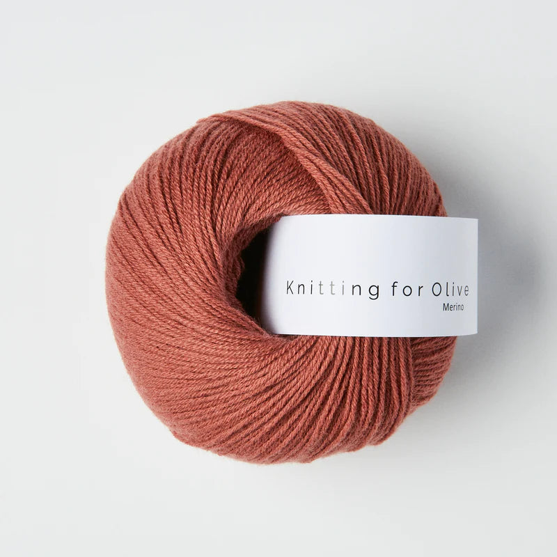 “Bol wol in de kleur ‘Plum Rose’ van Knitting for Olive, uit de Merino-lijn, netjes opgerold met wit label tegen een witte achtergrond – zacht, ademend en duurzaam garen.”