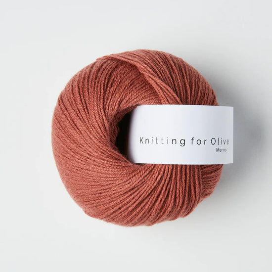 “Bol wol in de kleur ‘Plum Rose’ van Knitting for Olive, uit de Merino-lijn, netjes opgerold met wit label tegen een witte achtergrond – zacht, ademend en duurzaam garen.”