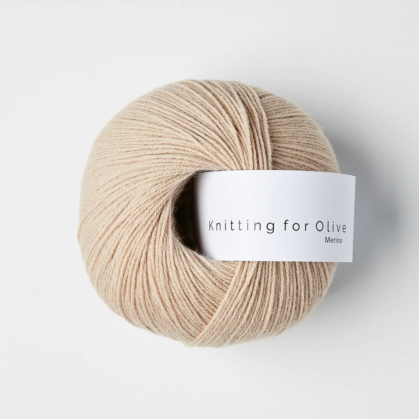 “Bol wol in de kleur ‘Powder’ van Knitting for Olive, uit de Merino-lijn, elegant opgerold met wit label tegen een witte achtergrond – zacht, licht en perfect voor fijne breiprojecten.”