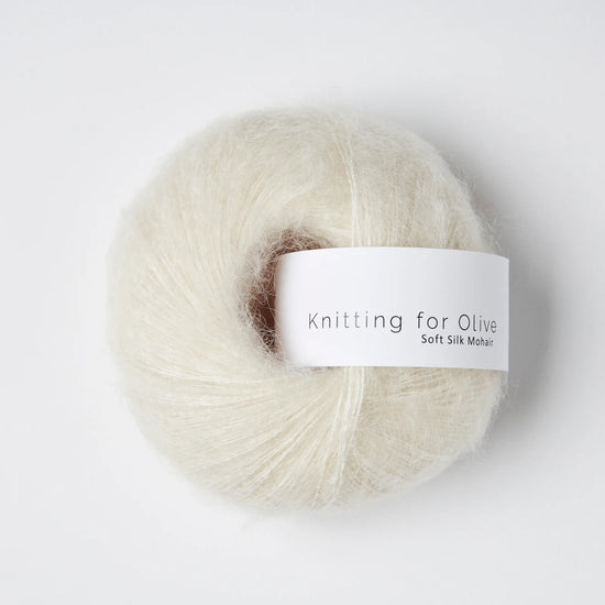 “Bol wol in de kleur ‘Cream’ van Knitting for Olive, uit de Soft Silk Mohair-lijn, luchtig en zijdeachtig opgerold met een wit label tegen een witte achtergrond – elegant en diervriendelijk garen in een zachte crèmetint.”