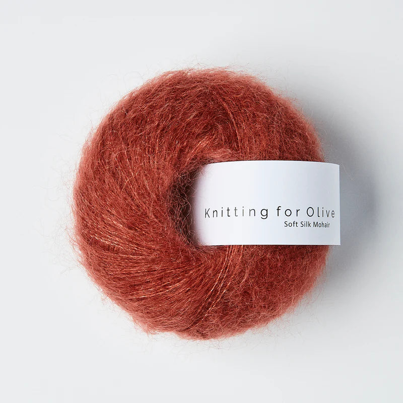 “Bol wol in de kleur ‘Forest Berry’ van Knitting for Olive, uit de Soft Silk Mohair-lijn, pluizig en luchtig opgerold met een wit label tegen een witte achtergrond – luxe en duurzaam garen van mohair en zijde.”