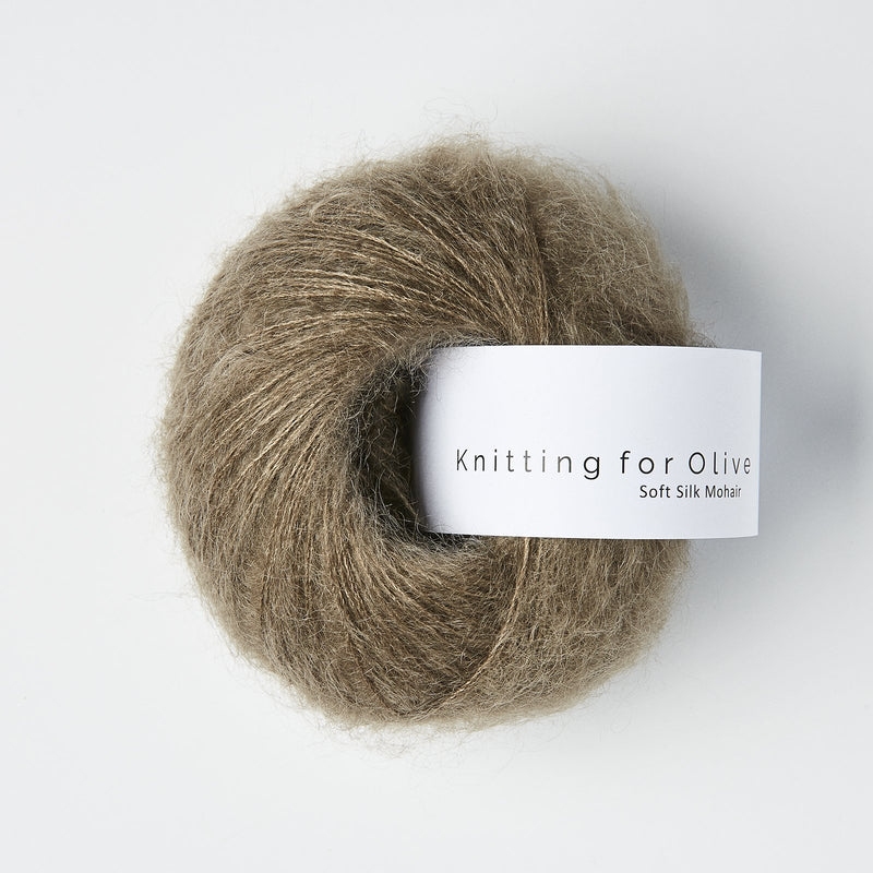 “Bol wol in de kleur ‘Hazel’ van Knitting for Olive, uit de Soft Silk Mohair-lijn, pluizig en luchtig opgerold met een wit label tegen een witte achtergrond – luxe en duurzaam garen van mohair en zijde.”
