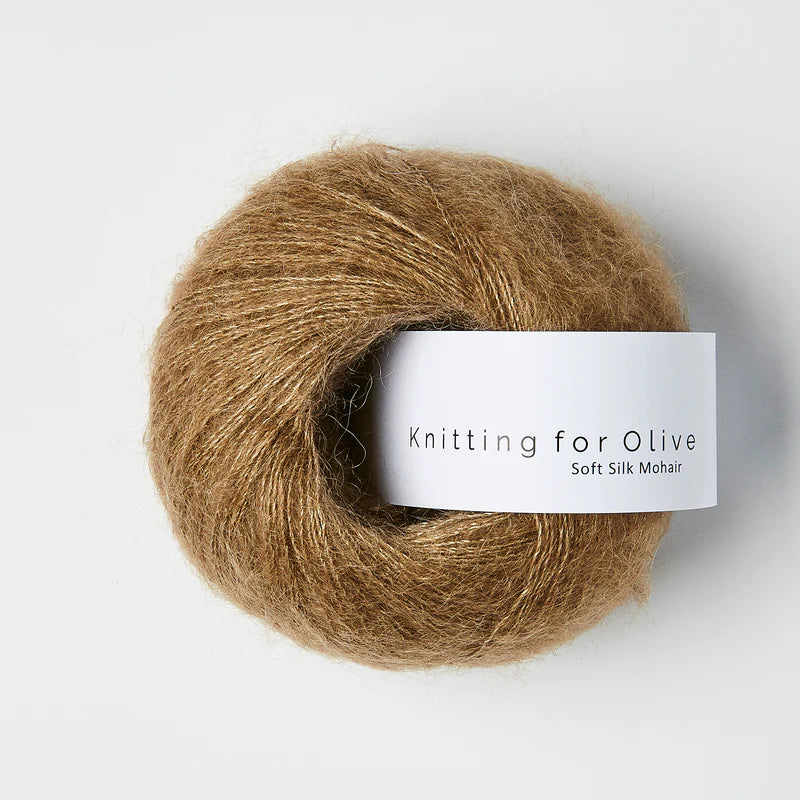 “Bol wol in de kleur ‘Nut Brown’ van Knitting for Olive, uit de Soft Silk Mohair-lijn, pluizig en luchtig opgerold met een wit label tegen een witte achtergrond – luxe en duurzaam garen van mohair en zijde.”