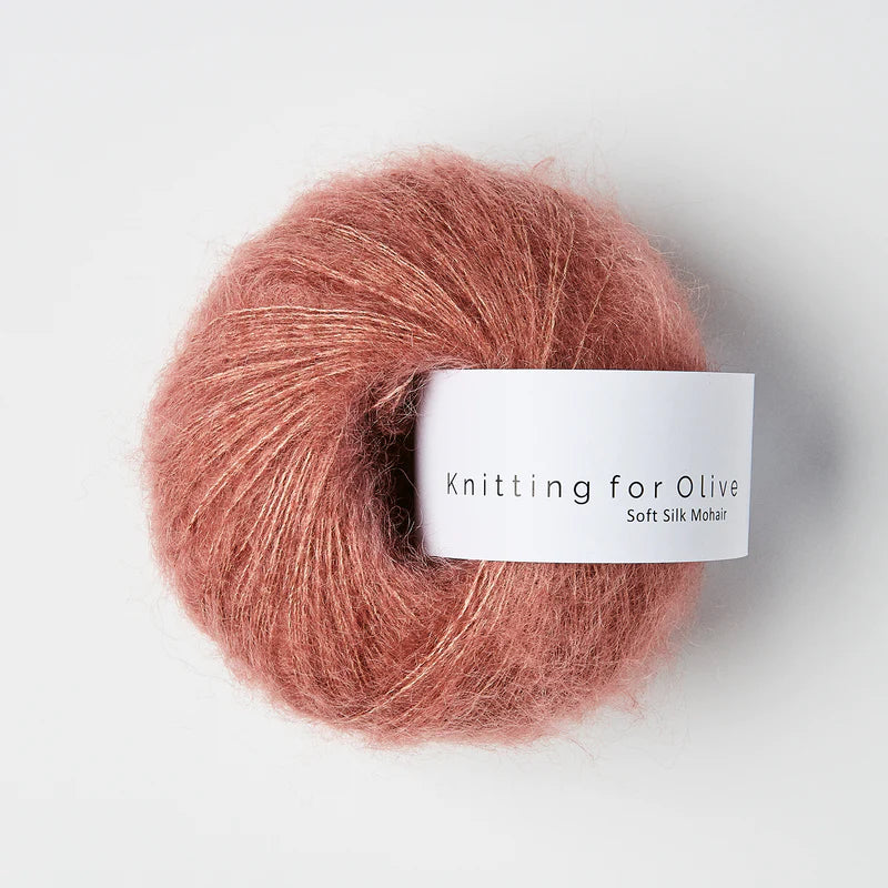 “Bol wol in de kleur ‘Plum Rose’ van Knitting for Olive, uit de Soft Silk Mohair-lijn, pluizig en luchtig opgerold met een wit label tegen een witte achtergrond – luxe en duurzaam garen van mohair en zijde.”