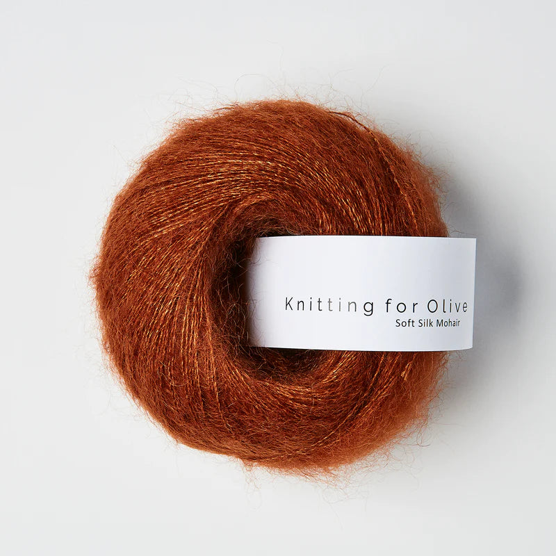 “Bol wol in de kleur ‘Rust’ van Knitting for Olive, uit de Soft Silk Mohair-lijn, pluizig en luchtig opgerold met een wit label tegen een witte achtergrond – luxe en duurzaam garen van mohair en zijde.”
