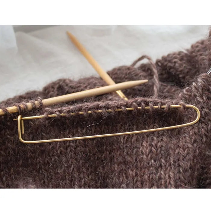 Seeknit Stitch Holder van goudkleurig aluminium in gebruik om steken tijdelijk vast te houden in een breiproject. Handige accessoire voor soepel breien.